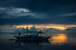 Boy pushing a bangka boat with a long pole in sunset