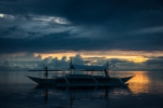 Boy standing on bow of bangka in sunset with long pole in his hands