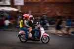 Three girls speeding by on a pinky-white scooter