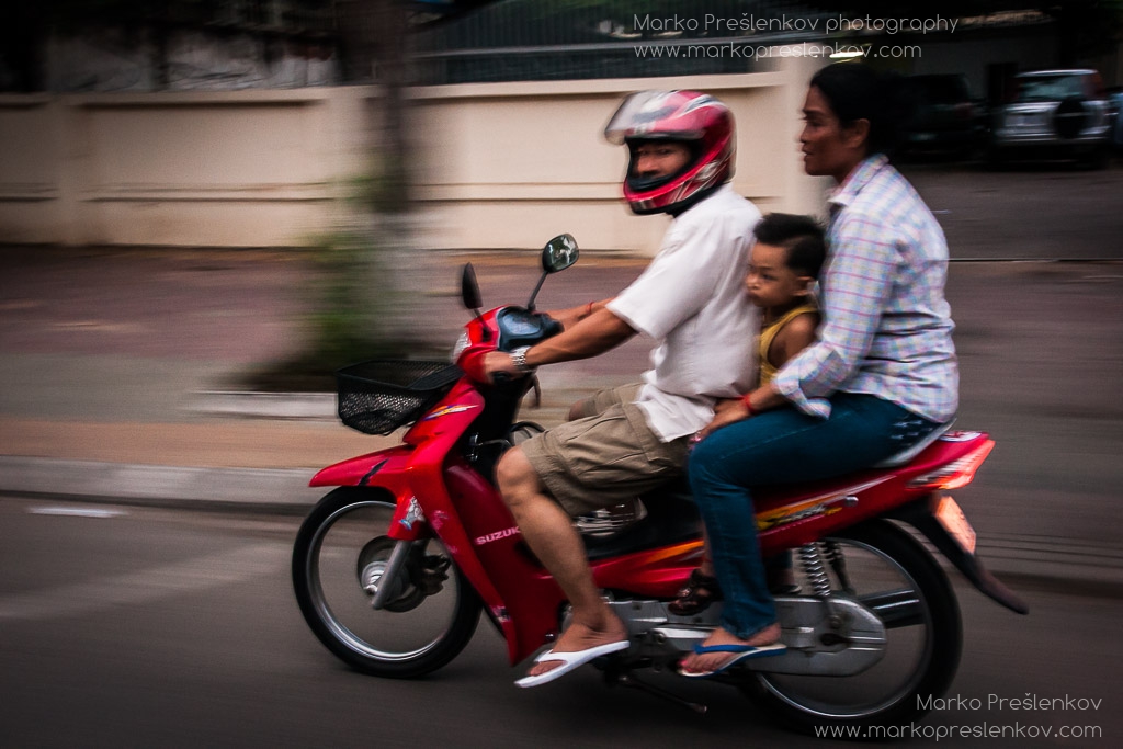 Family of three on a red Suzuki scooter